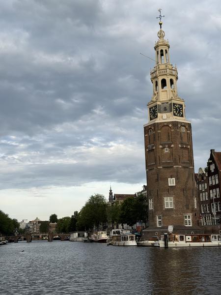 This photo captures a tranquil view of the 's-Gravenhekje and Rapenburg canal in Amsterdam, dominated by a historic brick clock tower under a cloudy sky